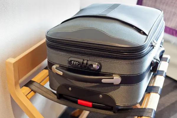 A gray suitcase on a suitcase stand in a hotel room keeping it off the ground and away from easy bed bug access.