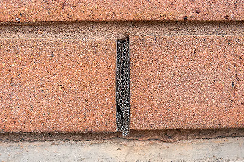 Metal weep hole covers installed in a brick wall by Arrow Environmental Services to allow ventilation while blocking pests.
