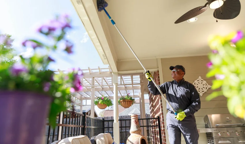 An Arrow Environmental Services technician using a long-reach duster to remove spider webs and wasp nests from a Florida patio ceiling.