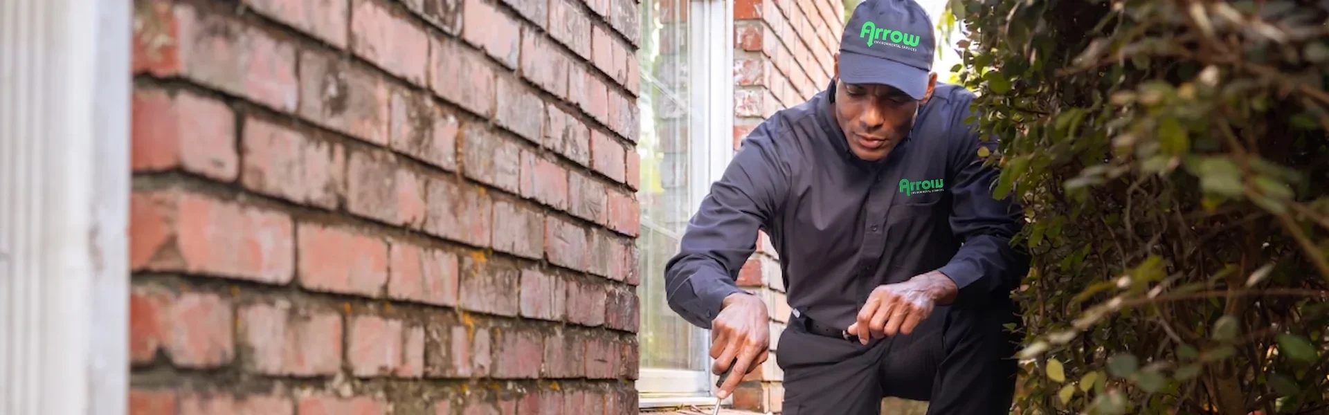 An Arrow Environmental Services technician inspecting a brick home’s foundation for pest entry points in the Florida area.