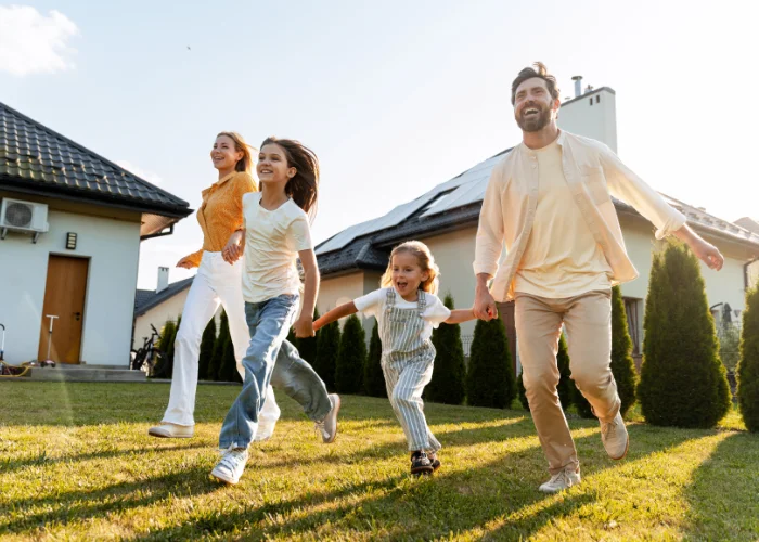 Parents and their two young daughters holding hands while running and smiling across a green suburban backyard.